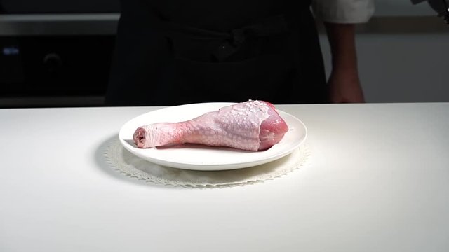 The chef salts the drumstick of a Turkey. Large salt falls from the hands of the cook on the meat. Slow motion.