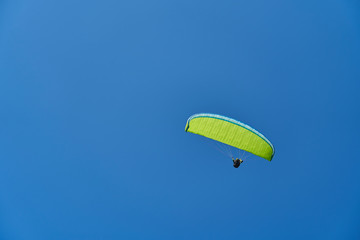 A paraglider with a yellow-green parachute sailing accros a clear, cloudless blue sky. Extreme, adrenaline sports. A lot of negative space for messages.