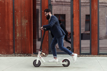 Bearded businessman riding to work on electric scooter
