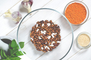 The bean diet. Beans, lentils, sesame garlic and basil in glass plates stand on a wooden table