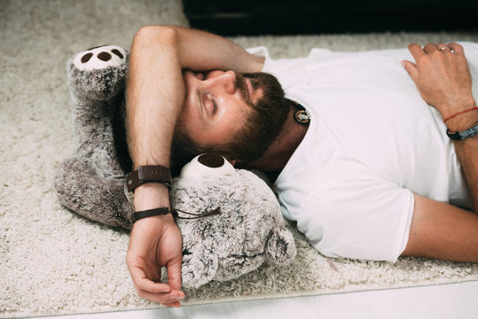 Bearded man sleeping on the floor on a soft toy, tired or drunk