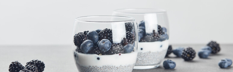 panoramic shot of tasty yogurt with chia seeds, blueberries and blackberries in glasses near...