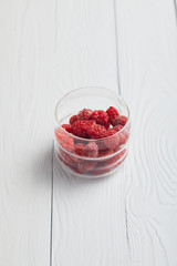 glass with fresh raspberries on white wooden table