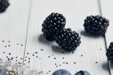 close up view of blackberries near scattered chia seeds on white wooden table