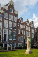 Naklejka premium Amsterdam, Netherlands - 06/14/2019: garden of Begijnhof with ancient buildings and Christ statue. Famous medieval yard with sculpture of Jesus Christ in Amsterdam. Religious heritage. 