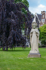 Amsterdam, Netherlands - 06/14/2019: garden of Begijnhof with ancient Jesus Christ statue. Famous medieval yard with sculpture of Jesus Christ in Amsterdam. Religious heritage. 