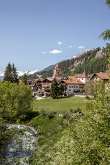 Fototapeta na wymiar View of a village in the swiss alps with meadows, mountains, cows, church and beautiful houses in spring at sunshine