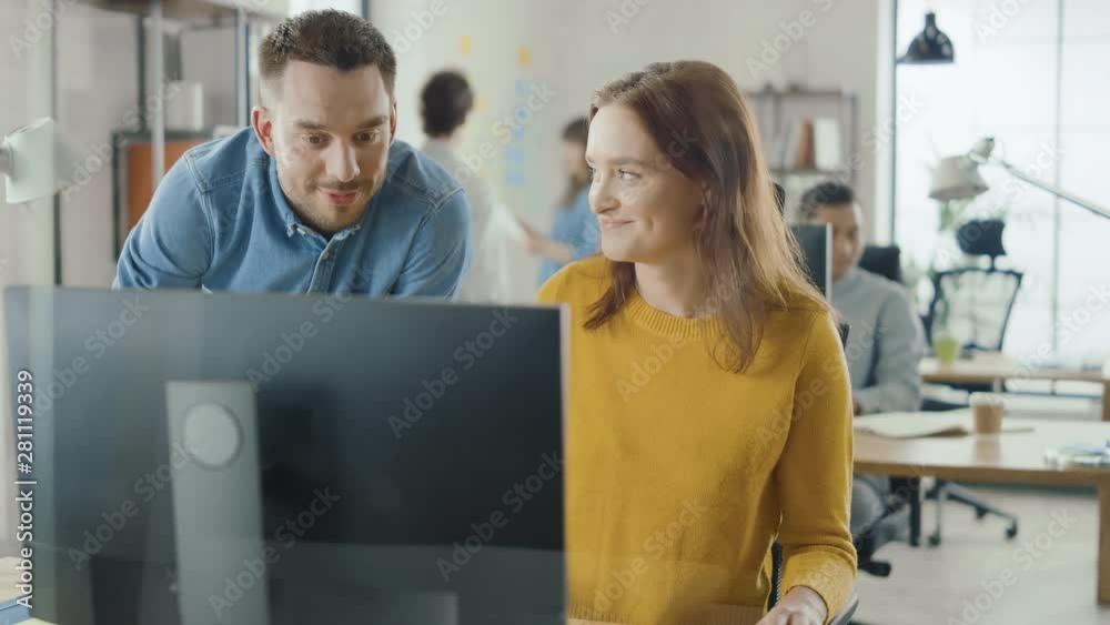Poster female specialist works on desktop computer, project manager stands beside and gives advice on optim