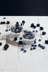 selective focus of glasses with yogurt and berries near scattered chia seeds isolated on black