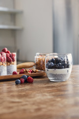 selective focus of glasses with yogurt, oat flakes and berries on wooden tray on table in kitchen