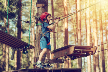 Boy in helmet is doing activity in adventure rope park with all climbing equipment.