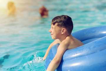 Portrait of European boy swimming in rubber ring in pool on summer vacation.