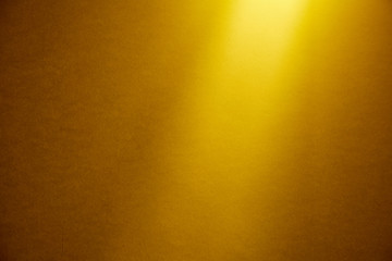 Fototapeta premium A light yellow beam of light illuminates from above a dark yellow finely textured background.