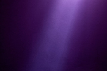 Violet ray of light illuminates a dark purple finely textured background