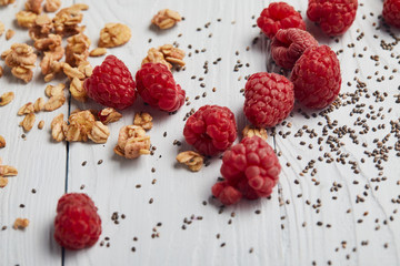 scattered raspberries, chia seeds and oat flakes on white wooden table