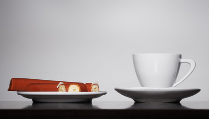 White coffee cup and plate with sweets on gray background
