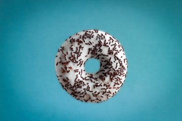 sweet donut with white chocolate icing and chocolate candy sprinkles flying on blue background