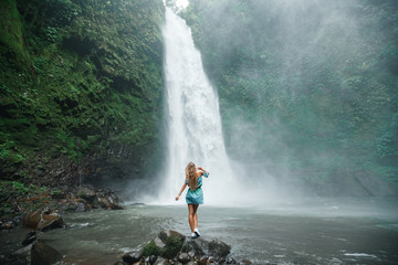 Back view young woman tourist enjoying tropical waterfall view in jungle