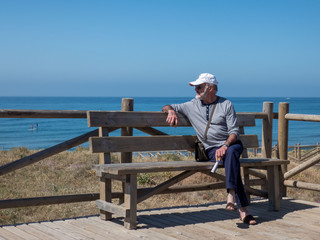 Fototapeta premium Old man on beach sitting on the bench looking at the sea