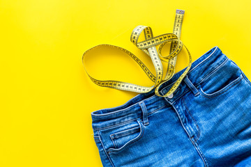 Trousers with measuring tape for weight loss and sport concept on yellow background top view space for text
