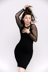 Fototapeta premium Horizontal Portrait of a pretty slim beautiful fashionable adult girl with beautiful brunette hair in a black dress. It should be in full growth, talking showing different poses and emotions