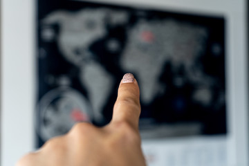 A female hand on the left points a finger at a blurred map of the world. Travel, communication.