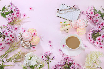Colorful flowers of pink phlox, cup of coffee and marshmallow with pastilla on a wooden table, top view with place for text, flat lay-out, selective focus. Pink flowers on wooden background