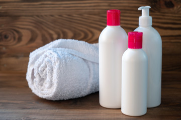 Obraz na płótnie Canvas Set of plastic white bottle with liquid cosmetic products for skin care of the face and body and a white towel on the wooden background.