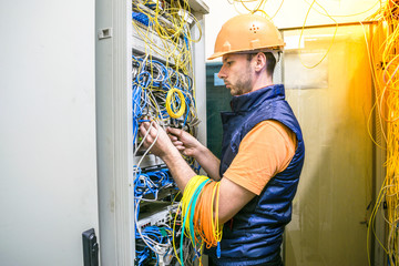 Signalman repairs internet connection. An engineer in an orange helmet mounts wires in a switching...