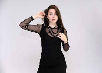 Fototapeta premium Portrait on white background of a pretty slim beautiful fashionable adult girl with beautiful brunette hair in a black dress. Standing talking demonstrating different poses and emotions