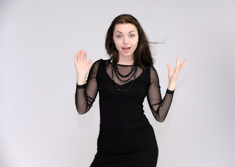 Portrait on white background of a pretty slim beautiful fashionable adult girl with beautiful brunette hair in a black dress. Standing talking demonstrating different poses and emotions