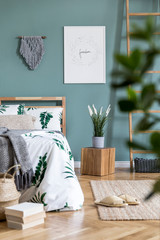 Stylish and design composition of bedroom interior with wooden bed, mock up poster frame, cube, ladder, plants, macrame and elegant accessories. Beautiful bed sheets, blanket and pillow. Template.
