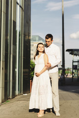 Young smiling couple walks around the city. A man gently embraces his pregnant wife. Germany,...