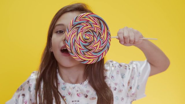 Happy child sucking lollipop on yellow background