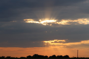 Beautiful sunset and dramatic clouds on the sky. Rays of light shining through dark clouds.