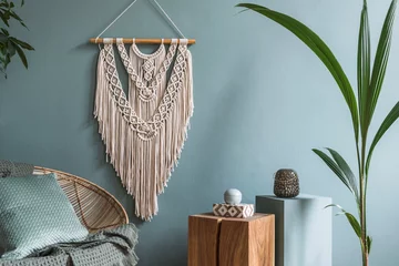 Fotobehang Boho Interior design of living room at modern home with stylish rattan armchair, pillows, plaid, beige macrame, wooden cubes, tropical plants and elegant accessories. Design home decor. Eucalyptus walls.  © FollowTheFlow