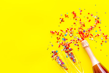Party with champagne bottle, glasses and colorful party streamers on yellow background top view space for text