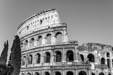 Obraz premium Black & white image of the ancient Colosseum, also know as Flavian Amphitheatre or Colosseo, an oval amphitheatre east of the Roman Forum with a clear sky in the historical city of Rome, Italy, Europe