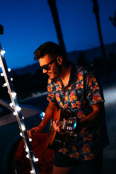 Young hawaiian man playing guitar for friends in a summer party on the beach.