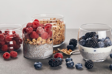 glasses with yogurt, berries and oat flakes near scattered berries on marble surface isolated on grey