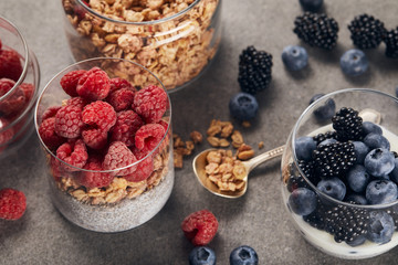 yogurt with chia seeds, oat flakes and raspberries near glass with yogurt and blueberries on marble surface