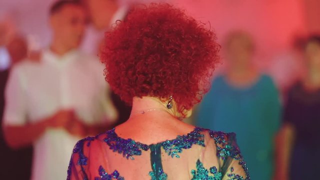 dancing elderly lady with bright red hair at a wedding in a festive hall