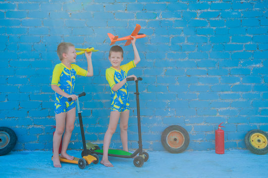 Happy blond children playing with bright plastic airplane against brick wall in swimsuit for boys. happy kids riding scooter on sunny summer day. concept of educational games for preschoolers