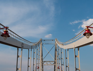 iron bridge with red modern city lanterns. deep perspective, bridge columns leads to blue sky on background.