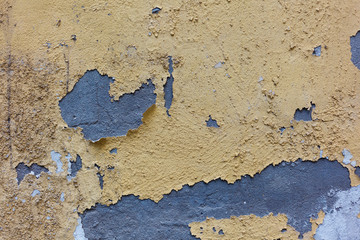 Old weathered painted wall background texture . Yellow dirty peeled plaster wall with falling off flakes of paint.