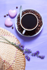 Obraz na płótnie Canvas A cup of coffee, lavender flowers, pink cookies and a piece of straw hat on a purple background is a gentle, summer, rural design concept with space for text.