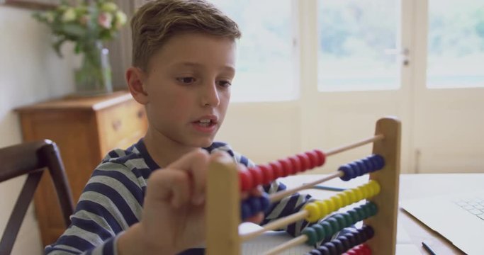 Boy learning mathematics on abacus at table in a comfortable home 4k