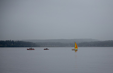 A Bright Yellow and Orange Sailboat in a murky, grey day in Puget Sound