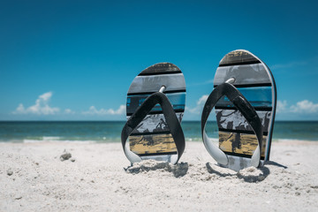 Pair of Flip flops in white beach sand with blue ocean at background. Perfect day at vocations 