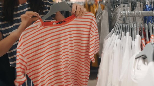 Woman buys new t-shirts for summer. Woman in clothing store looking for new clothes.